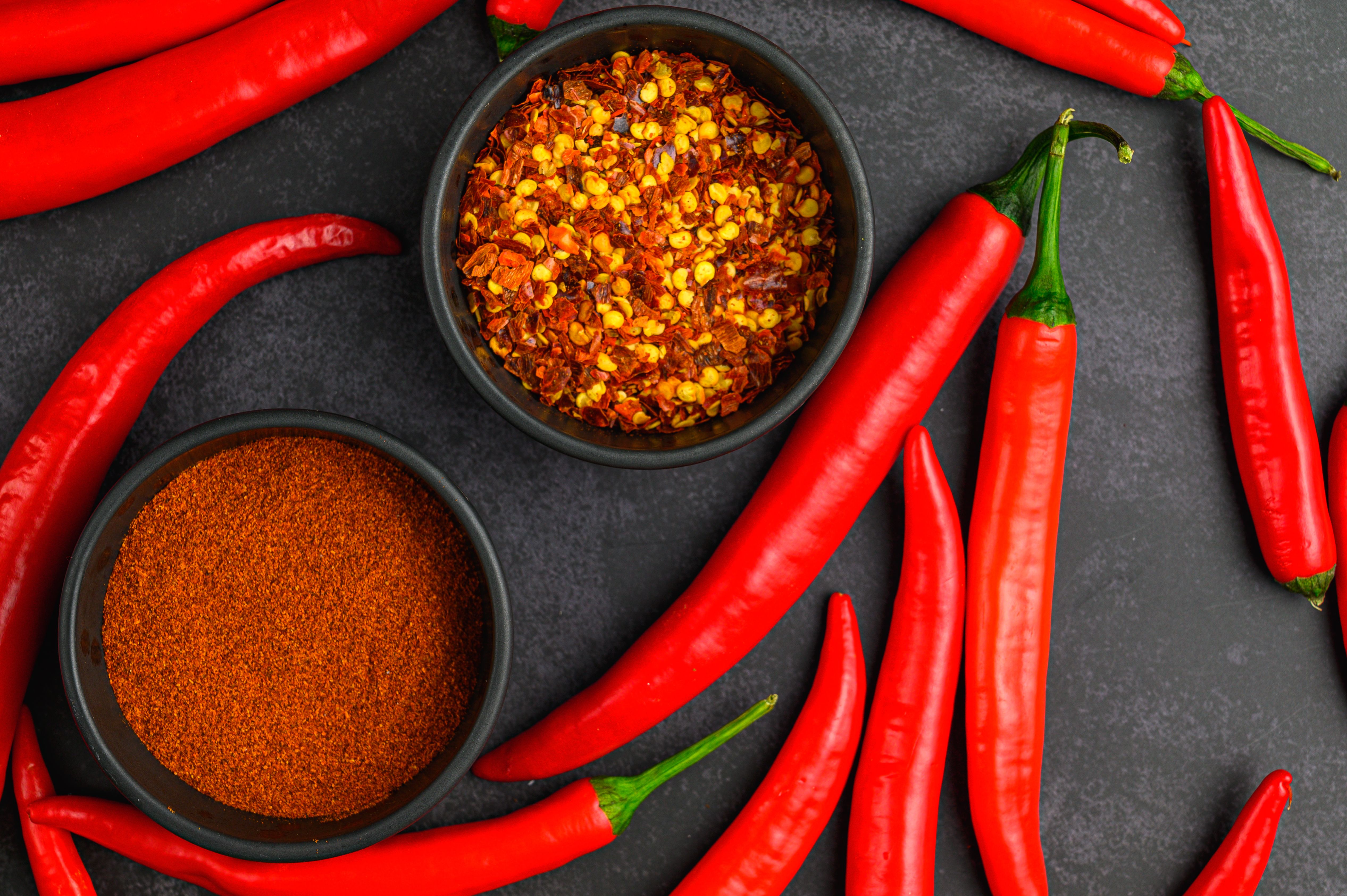 Bowls of chili flakes and chili powder beside whole red chilies